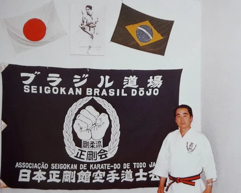 Tada Sesnei ao lado da bandeira da Seigokan do Brasil