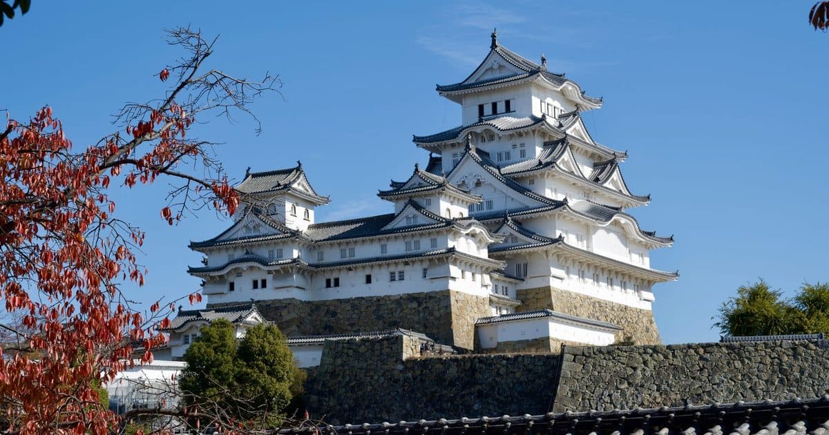 Himeji Castle with its traditional Japanese architecture set against a clear blue sky and autumn leaves.