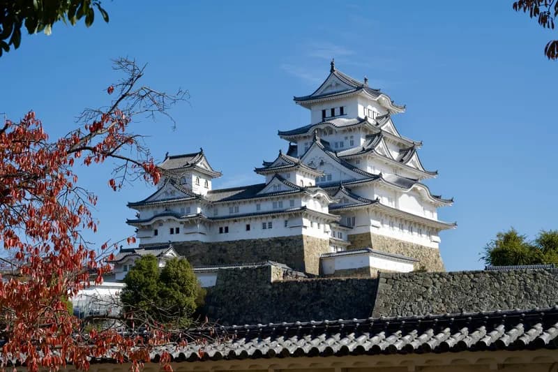 Himeji Castle with its traditional Japanese architecture set against a clear blue sky and autumn leaves.